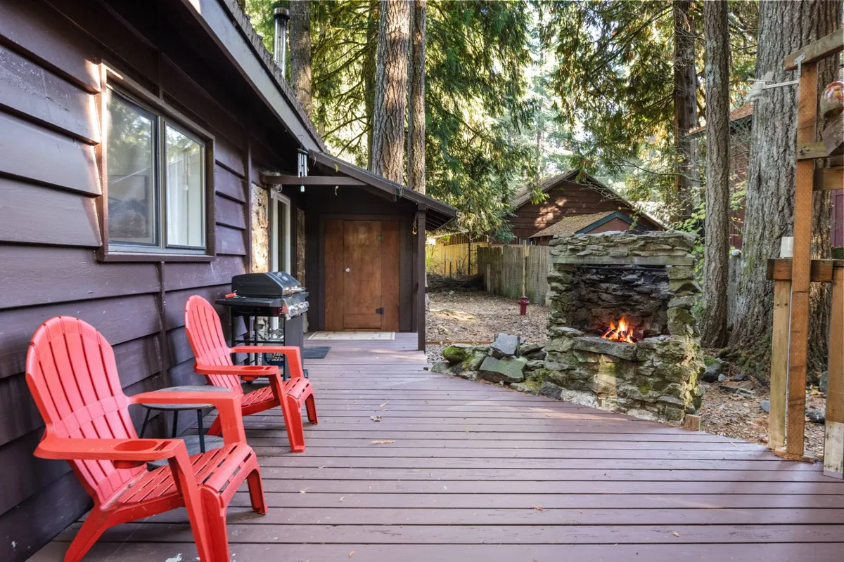 An inviting outdoor living space with red chairs set around a stone fireplace and grill. The area is positioned to take in the glow of sunset and is surrounded by natural scenery, suggesting a seamless connection between relaxation and the outdoors.