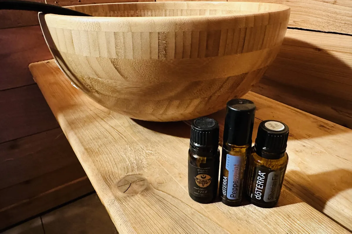 A wooden bowl and several essential oil bottles are arranged on a smooth wooden surface, hinting at aromatherapy and relaxation rituals. The setup evokes soothing, spa-like experiences and a calming atmosphere.
