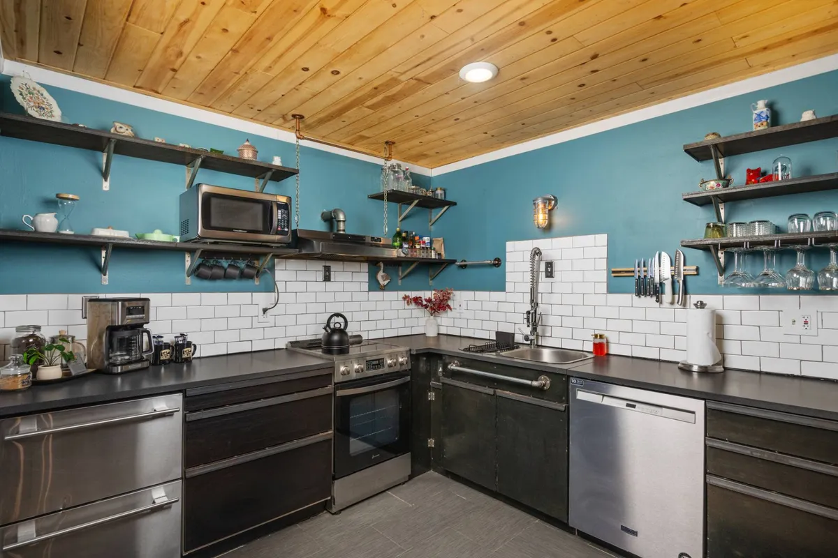A modern kitchen with stainless steel appliances, open shelving adorned with decorative items, and a sleek black countertop. The space is both functional and open, ideal for group meal prep, entertaining, or casual conversation while cooking.