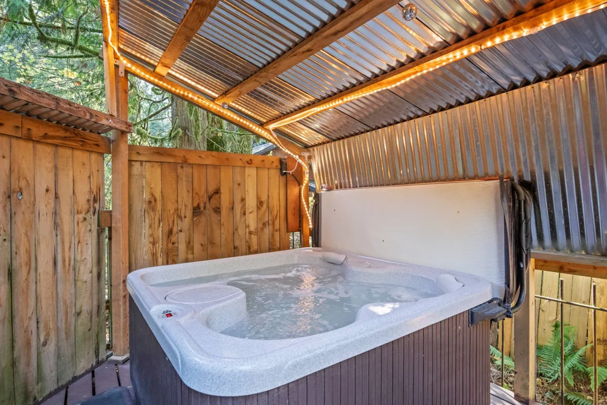 A tranquil interior scene featuring a private hot tub set against warm wooden walls, illuminated by soft ambient lighting. The space invites relaxation, with the promise of stargazing and the soothing sounds of the surrounding forest just beyond.