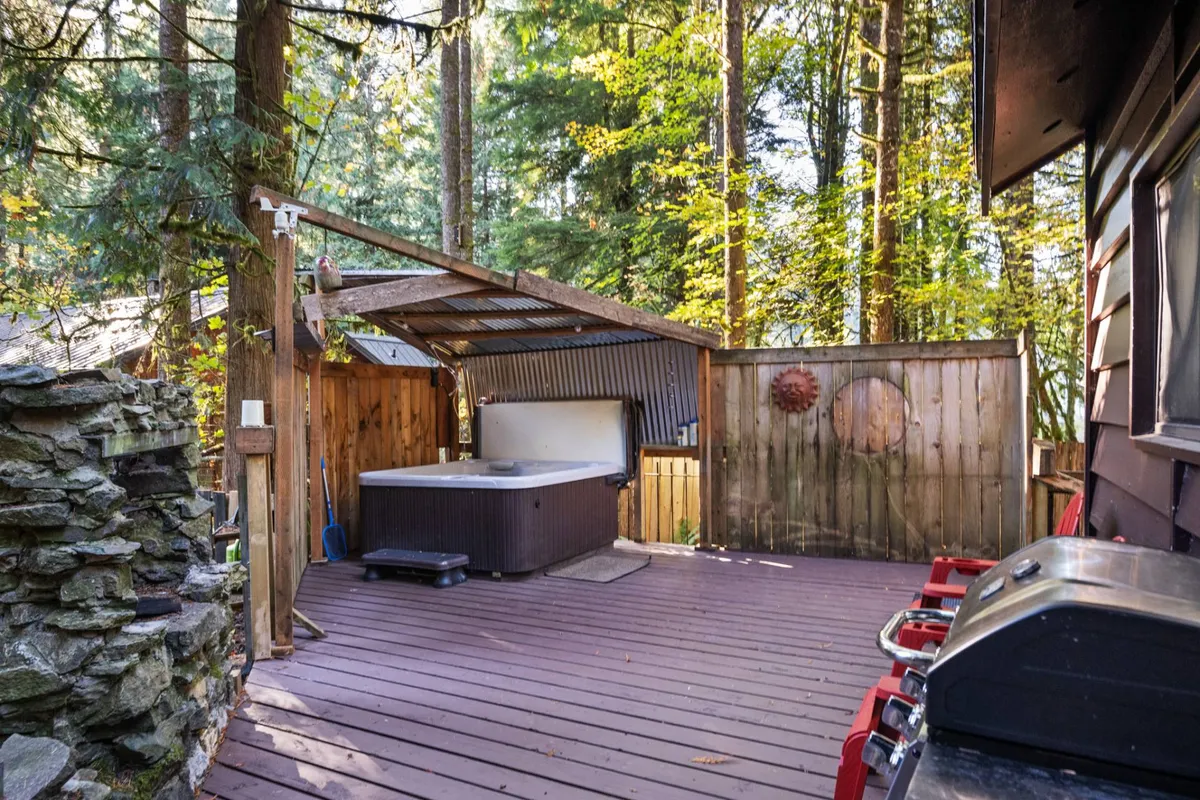 This exterior shot features a wooden deck nestled among trees, with a hot tub, grill, and inviting outdoor seating. The natural setting is tranquil, perfect for relaxing with pets or prepping for a day out.
