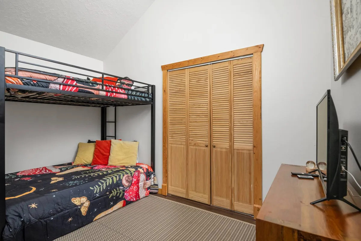 A playful bunk room featuring a wooden bunk bed with colorful bedding and a wooden closet. The space feels inviting and fun, suitable for children or groups, and provides a sense of togetherness and adventure.