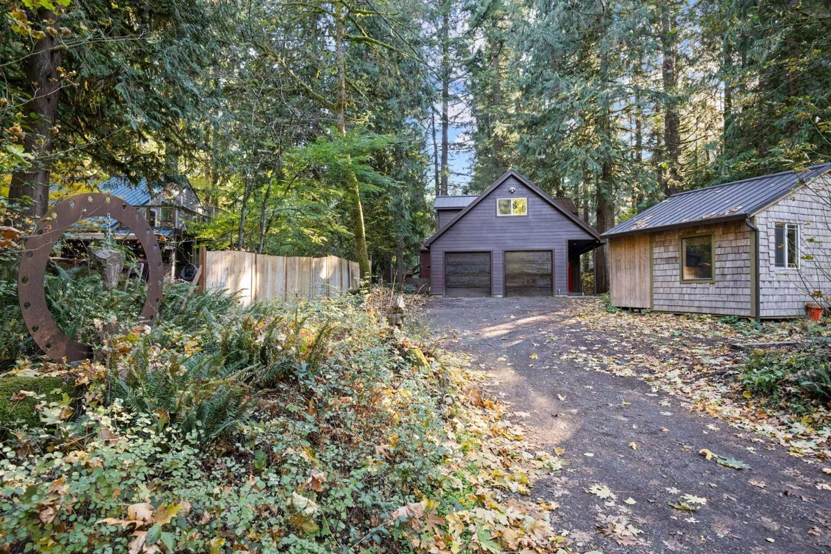 A peaceful exterior view of the main house, surrounded by towering trees and a spacious driveway. The image hints at the property's natural setting and easy access, with enough parking for RVs or trailers and space for storing gear.