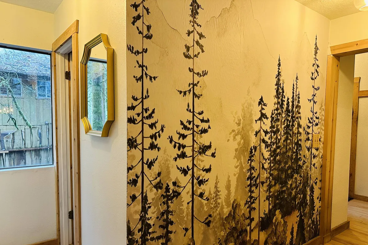 A tranquil hallway features a wall mural depicting lush, towering trees, complemented by a mirror and warm wooden trim. The soft lighting and nature-themed decor evoke a sense of serenity and connection to the surrounding forest environment.
