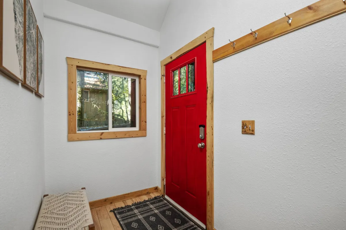 A warmly lit entryway featuring a red front door, a wooden window frame, a decorative bench, and wall hooks, setting the tone for a welcoming arrival. The space is ideal for transitioning from outdoor adventures to the comfort of the home, and suggests a gathering place where families and groups begin and end their explorations.